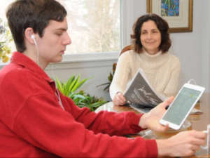 Woman holds newspaper looking at younger man hold an ereader with headphones