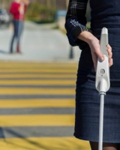 Close up of woman holding Smart Cane in right hand while standing in crosswalk.