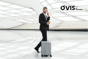 Man in black suit walks in airport with silver suitcase next to him.  He is not touching suitcase.